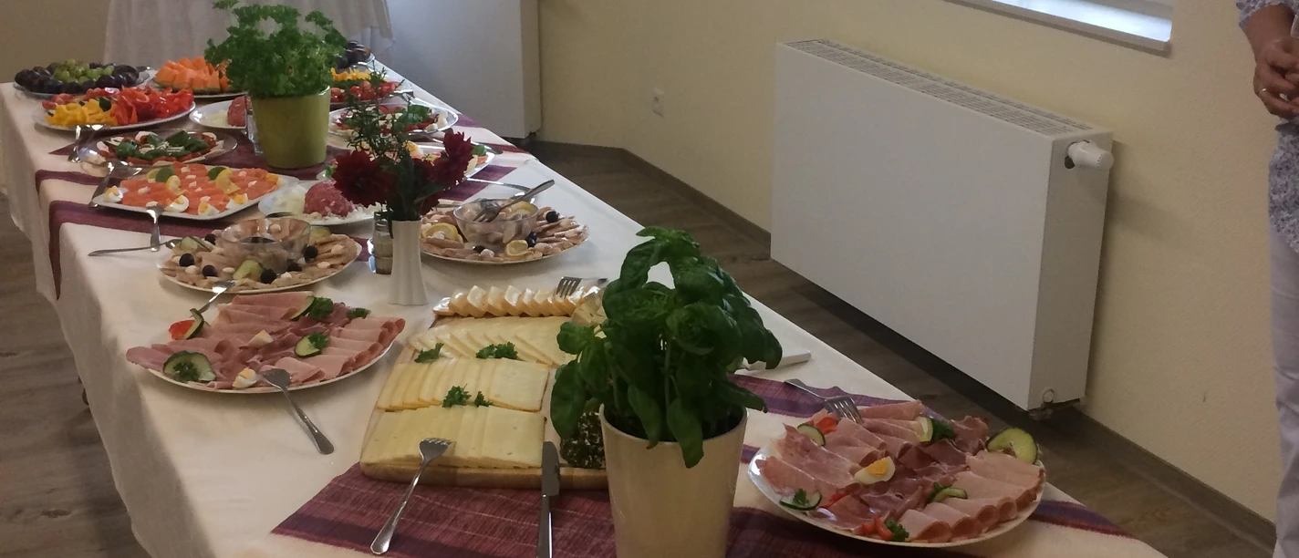 Seniorenfrühstück Ein langer Frühstückstisch mit Wurstplatten, Käse und frischen Kräutern auf weißen Tischdecken.