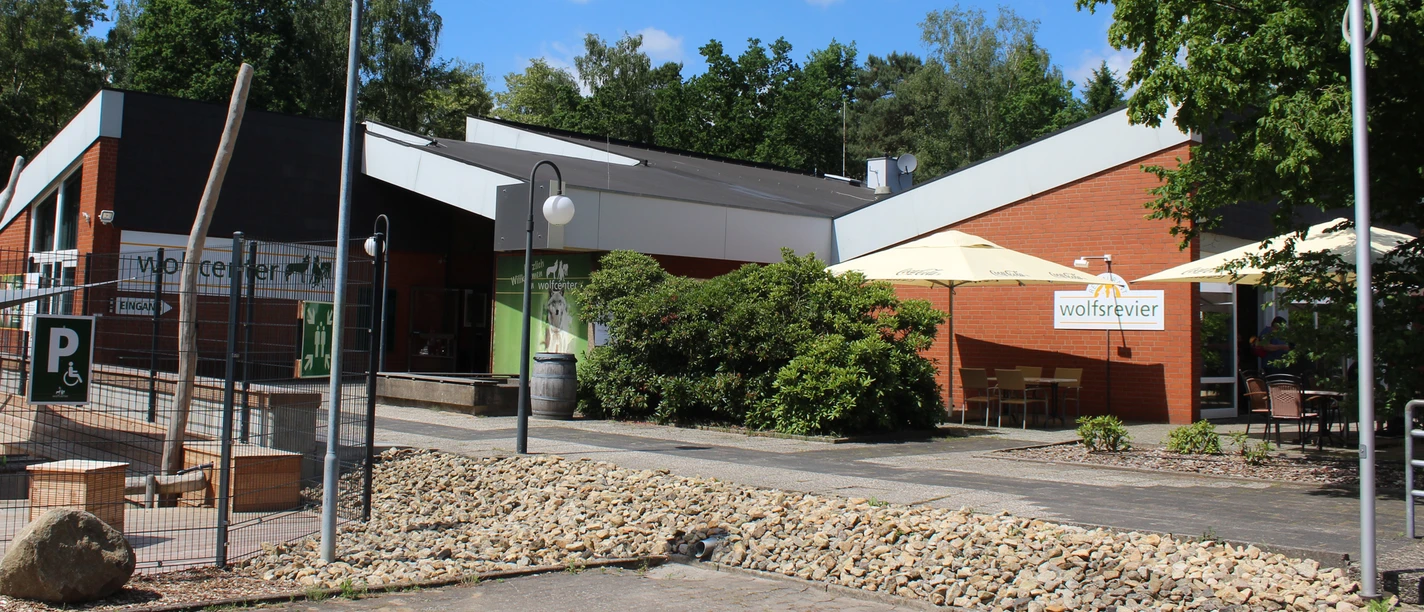 Modern entrance area of the Wolfcenter with green areas, covered seating and blue sky.
