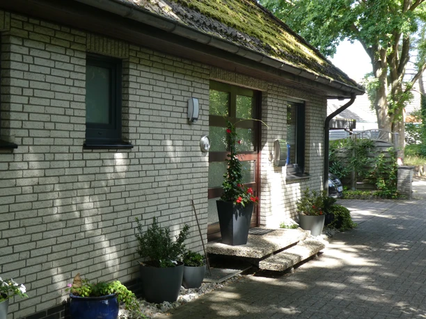 Entrance to a guesthouse with a paved path, plants in pots and a large window at the front of the house.