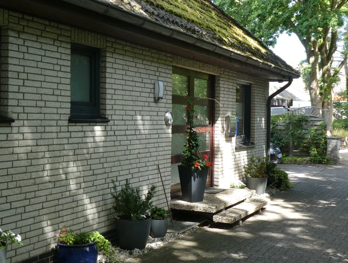 Radler-Pension Bormann Eingang einer Pension mit gepflastertem Weg, Pflanzen in Töpfen und großem Fenster an der Hausfront.