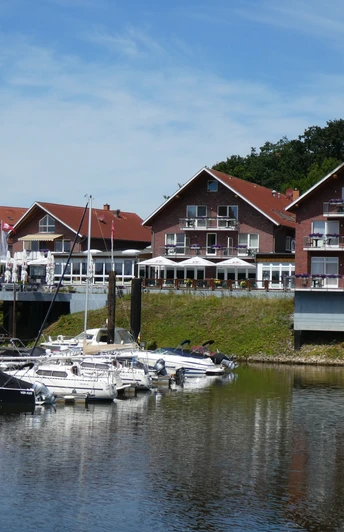 Ein Hotel-Restaurant mit roten Backsteinwänden am Ufer, umgeben von Booten am ruhigen Wasser.