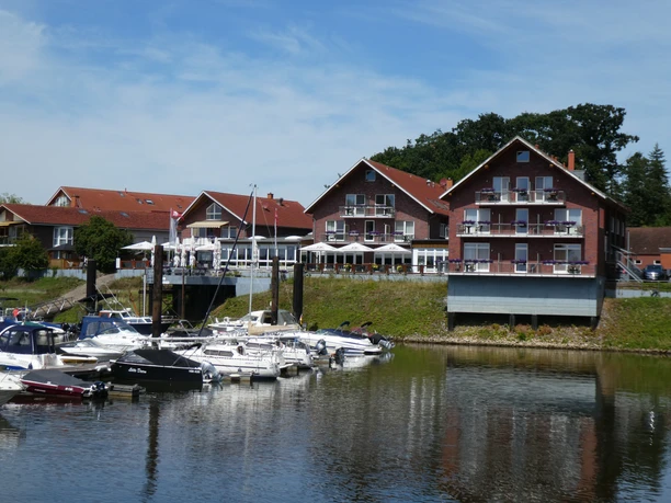 Hotel-Restaurant Bootshaus Ein Hotel-Restaurant mit roten Backsteinwänden am Ufer, umgeben von Booten am ruhigen Wasser.