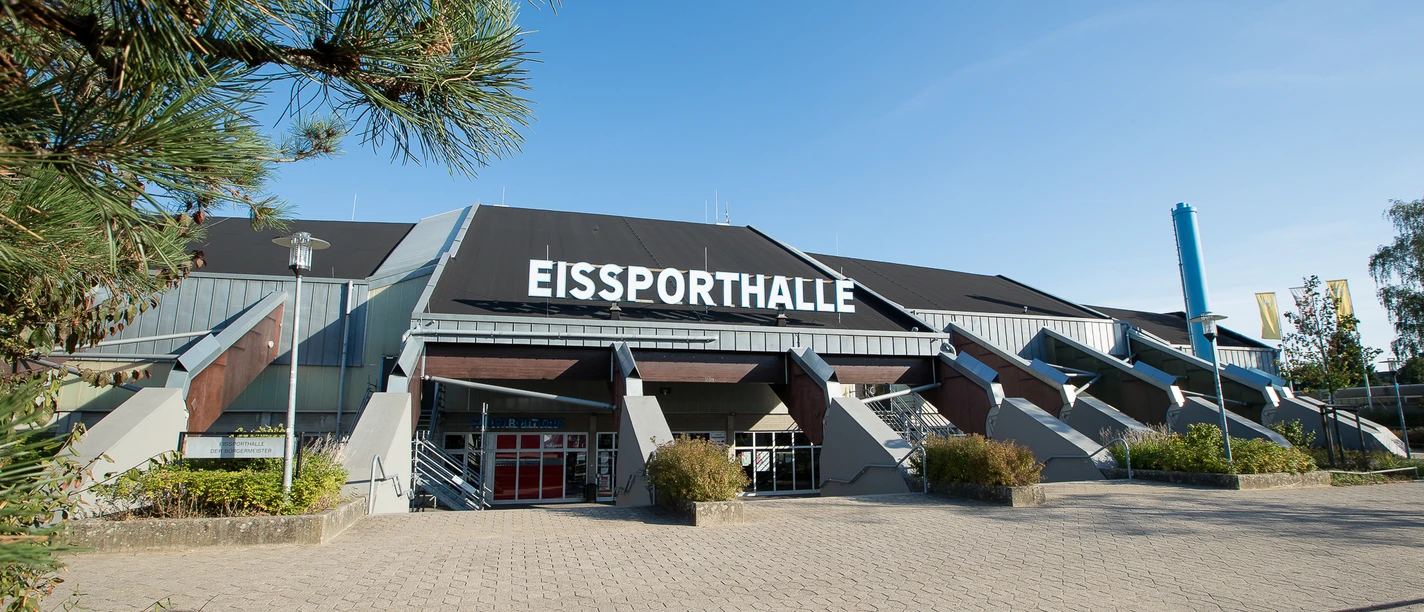Eissporthalle Ratingen Große Eissporthalle in Ratingen mit markantem Dach, umgeben von Pflanzen und einem gepflasterten Vorplatz.