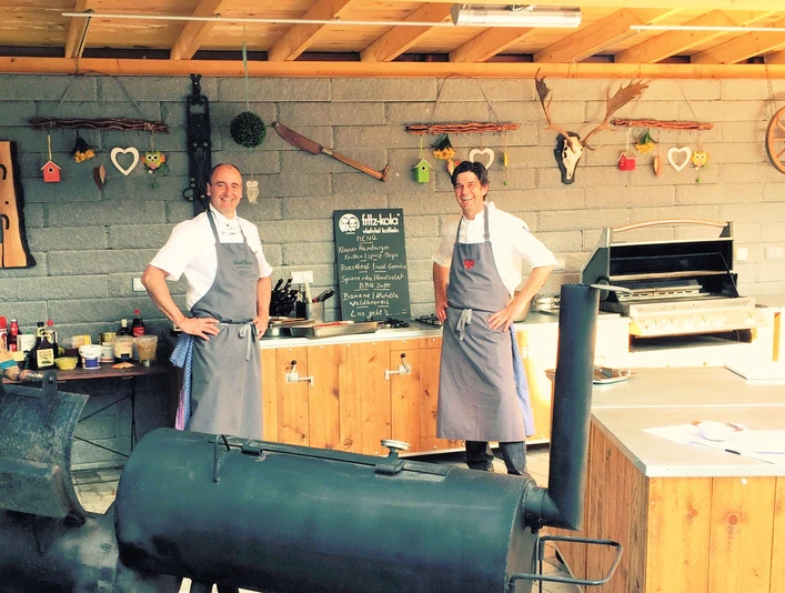 Außenküche in der Kleinen Schweiz, Velbert Zwei Personen in Schürzen stehen in einer rustikalen Außenküche mit Grill und Dekorationen.