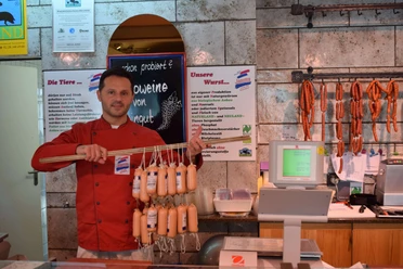 Naturfleischerei Janutta in Velbert Fleischer in roter Jacke präsentiert stolz eine Vielzahl an frischen Würsten in traditioneller Metzgerei.