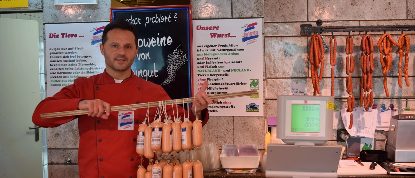 Naturfleischerei Janutta in Velbert Fleischer in roter Jacke präsentiert stolz eine Vielzahl an frischen Würsten in traditioneller Metzgerei.