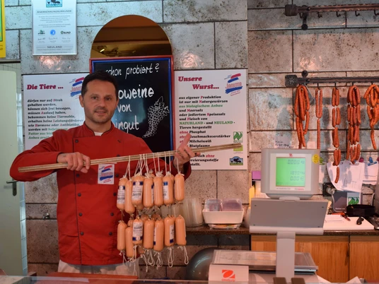 Naturfleischerei Janutta in Velbert Fleischer in roter Jacke präsentiert stolz eine Vielzahl an frischen Würsten in traditioneller Metzgerei.