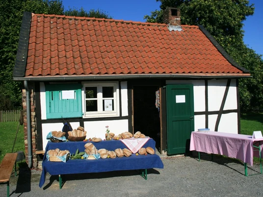 Brot backen im Historischen Backhaus in Erkrath Traditionelles Fachwerkgebäude mit Ziegeldach, Brote auf blauen Tischflächen im Freien vor dem Haus.