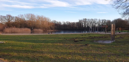 Badesee Mindenerwald Ein ruhiger Badesee mit Sandstrand und Spielplatz, umgeben von Bäumen und grasbewachsenen Ufern.