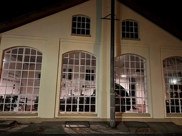 Dampfmaschine An illuminated building at night, machines are visible inside through large windows.