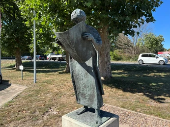 Der Zeitungsleser Bronzestatue eines Mannes liest stehend eine offene Zeitung neben Straße und grünen Bäumen.