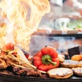 Grillakademie in der Marienburg in Monheim am Rhein Verschiedene Gemüsesorten braten auf einem großen Grill feurig, darunter rote Paprika und Zwiebeln.