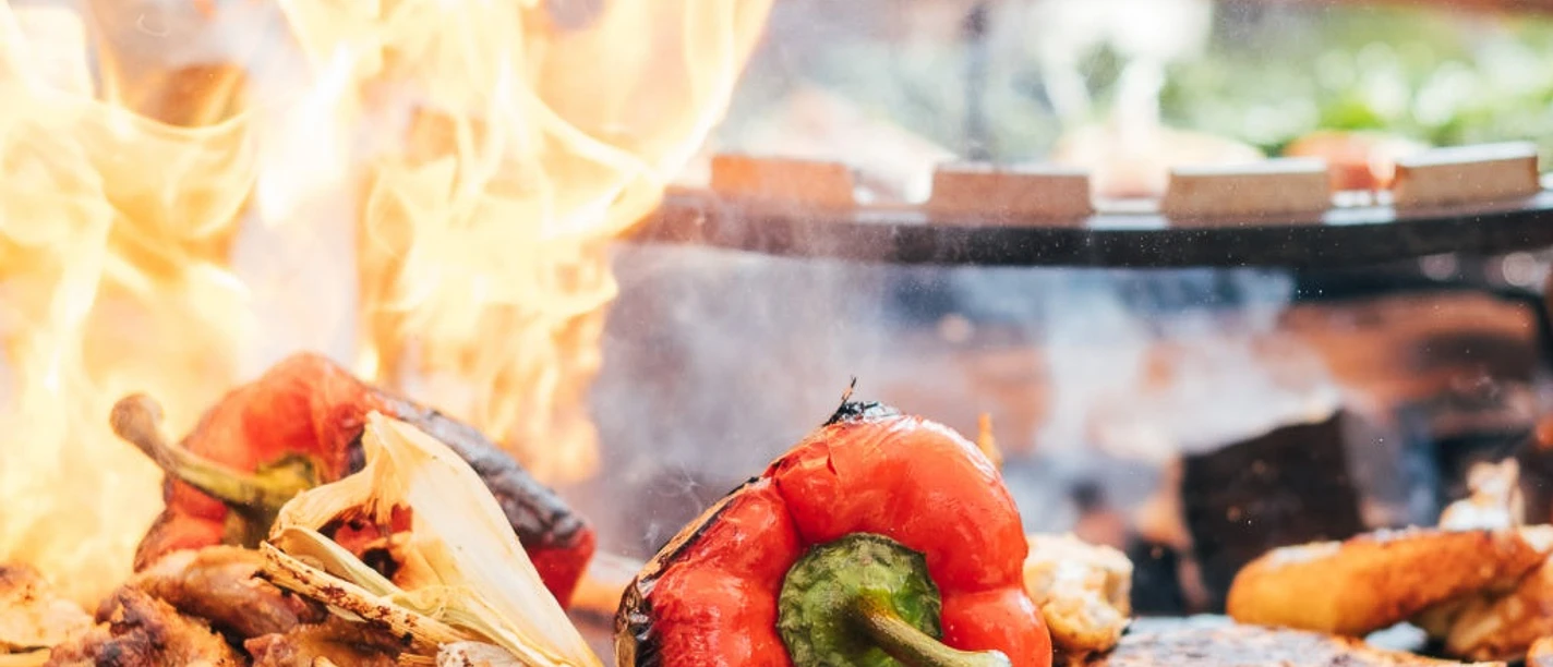 Grillakademie in der Marienburg in Monheim am Rhein Verschiedene Gemüsesorten braten auf einem großen Grill feurig, darunter rote Paprika und Zwiebeln.