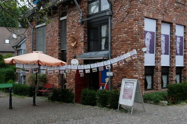 Cafe Im Dorf in Haan-Gruiten Ein Café mit roter Backsteinfassade, schattenspendendem Sonnenschirm und dekorativen Girlanden.