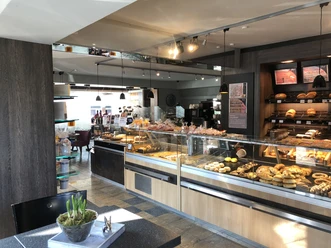 Droste Cafe, Konditorei u. Catering in Ratingen Ein helles Cafe mit Theken voller Gebäck und Kuchen, umgeben von modernem Interieur und Sitzplätzen.