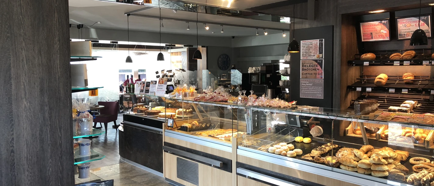 Droste Cafe, Konditorei u. Catering in Ratingen Ein helles Cafe mit Theken voller Gebäck und Kuchen, umgeben von modernem Interieur und Sitzplätzen.