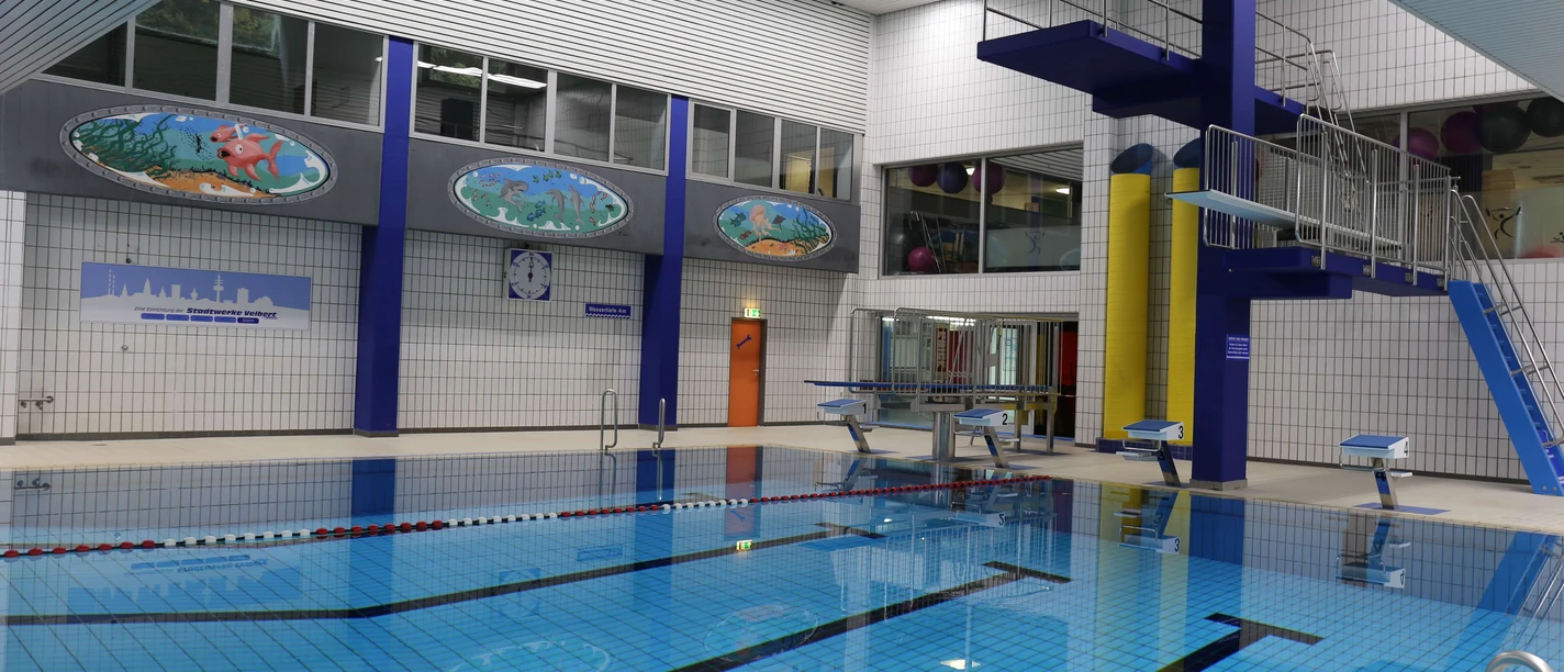 Nizzabad bei Velbert-Langenberg Ein modernes Hallenbad mit klar strukturiertem Becken, Leitern, Sprungturm und farbenfrohen Wandbildern.