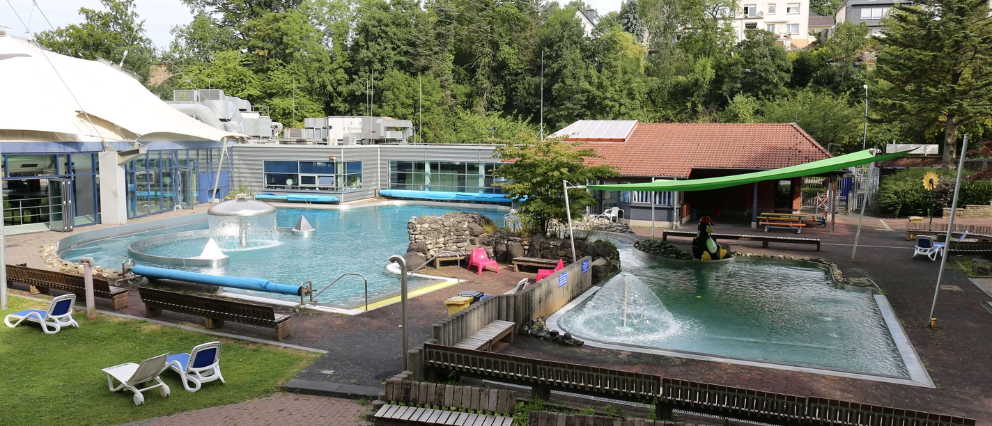 Parkbad in Velbert Ein Freibad mit zwei Pools und Sprungturm, umgeben von Bäumen und Liegestühlen in Velbert.