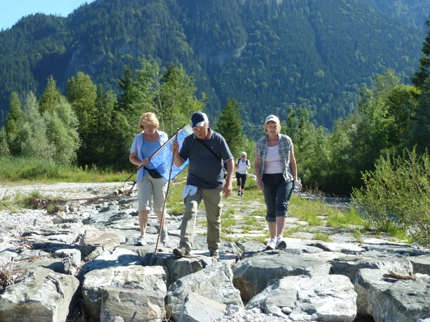 Pilgerwandern in der Zugspitz Region Eine Gruppe älterer Wanderer überquert felsiges Gelände in einer waldreichen Berglandschaft.