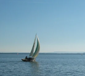 Wassersport Segelboot mit buntem Segel gleitet bei blauem Himmel über einen ruhigen, weitläufigen See.