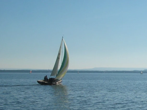 Wassersport Segelboot mit buntem Segel gleitet bei blauem Himmel über einen ruhigen, weitläufigen See.