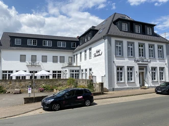 Weißes, zweistöckiges Gebäude mit Schieferdach und Hotel-Riesenbeck-Logo, davor ein geparktes Auto.