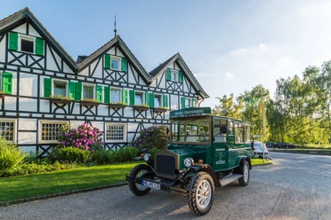 Lohmanns Romantik Hotel Gravenberg in Langenfeld Historisches Hotel mit grünen Fensterläden und Oldtimer im Vordergrund, umgeben von Landschaft.