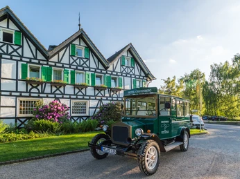 Lohmanns Romantik Hotel Gravenberg in Langenfeld Historisches Hotel mit grünen Fensterläden und Oldtimer im Vordergrund, umgeben von Landschaft.