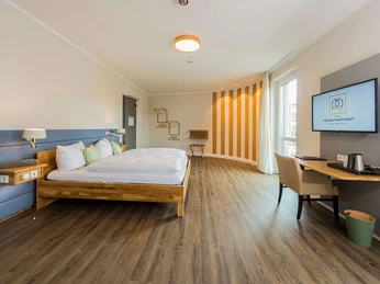 Hotel Neues Pastorat in Heiligenhaus Modernes Hotelzimmer im Neuen Pastorat, Heiligenhaus, mit Holzfußboden und stilvoller Einrichtung.