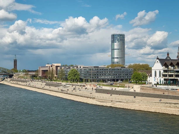Das Bild zeigt den KölnTriangle mit dem Rhein im Vordergrund und einem klaren Himmel.