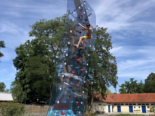 Waldfreibad Espelkamp Ein Junge klettert an einer durchsichtigen Kletterwand über einem Schwimmbecken im Waldfreibad Espelkamp.