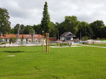 Grünes Freibadgelände mit Rutschen, großen Wiesenflächen und einem kleinen Gebäude im Hintergrund.