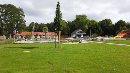 Waldfreibad Espelkamp Grünes Freibadgelände mit Rutschen, großen Wiesenflächen und einem kleinen Gebäude im Hintergrund.
