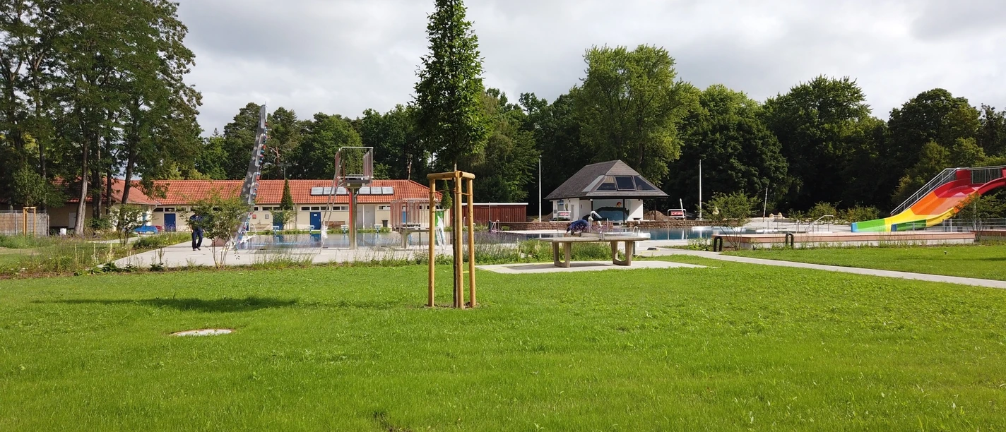 Waldfreibad Espelkamp Grünes Freibadgelände mit Rutschen, großen Wiesenflächen und einem kleinen Gebäude im Hintergrund.