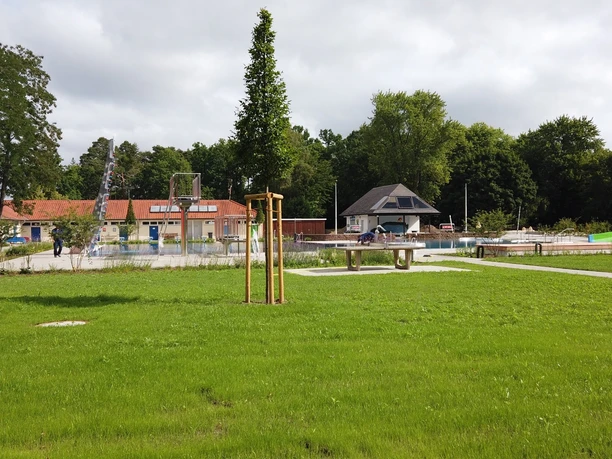 Waldfreibad Espelkamp Grünes Freibadgelände mit Rutschen, großen Wiesenflächen und einem kleinen Gebäude im Hintergrund.