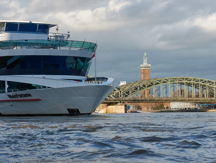 Köln-Düsseldorfer Deutsche Rheinschiffahrt Ein modernes Flusskreuzfahrtschiff der Köln-Düsseldorfer passiert malerisch die Rheinbrücke mit ihrem prägnanten Bogen und den angrenzenden, markanten Bauten im Hintergrund.A modern river cruise ship operated by Köln-Düsseldorfer passes picturesquely over the Rhine bridge with its striking arch and the adjacent, striking buildings in the background.