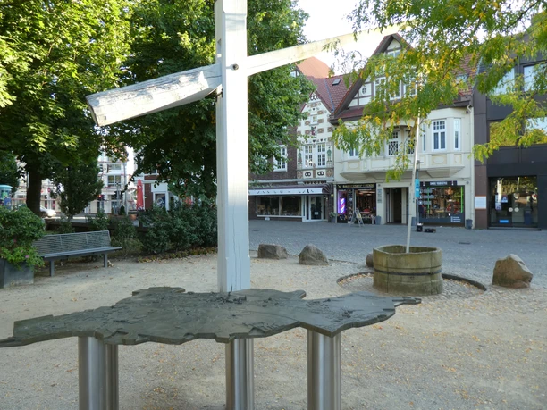 A bronze model of the town of Achim, displayed in a town square with historic buildings in the background.