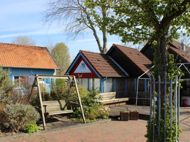 Seglertreff Otterndorf Einladender Imbiss Seglertreff Otterndorf mit Holzterrasse und Schaukel unter Bäumen.