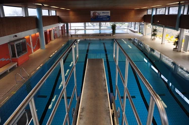 hallenbad luebbecke Blick auf ein Hallenbad mit Sprungturm, hellem Raum, großen Fenstern und einem Schwimmbecken.