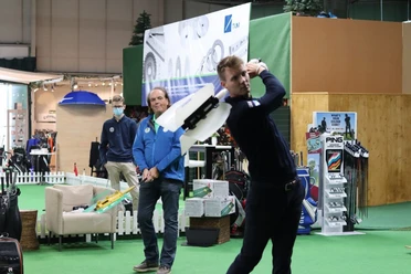 Indoorgolf bei Team Spieckerhoff in Langenfeld Personen spielen in einer Indoor-Golfanlage. Einer schwingt gerade den Schläger, im Hintergrund Golfzubehör.