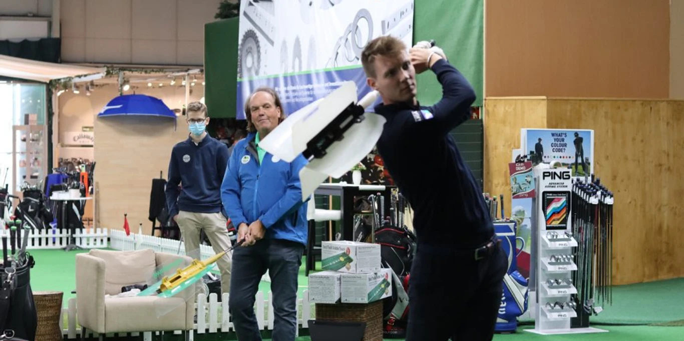 Indoorgolf bei Team Spieckerhoff in Langenfeld Personen spielen in einer Indoor-Golfanlage. Einer schwingt gerade den Schläger, im Hintergrund Golfzubehör.
