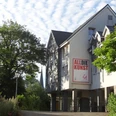 ALLDIEKUNST im Kunsthaus Velbert-Langenberg Ein Kunstzentrum in hellem Gebäude, umgeben von grünen Bäumen und einem klaren blauen Himmel.