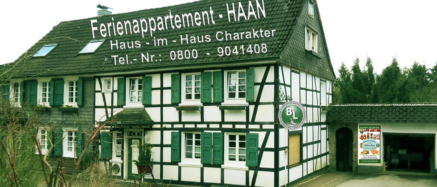 Ferienappartement Haaa Fachwerkhaus mit grünen Fensterläden und Werbeschrift in ländlicher Umgebung. Parkplatz davor.