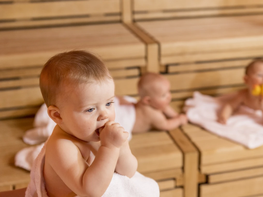 SWO_BabySauna_132.jpg Drei Babys entspannen auf Holzbänken in einer Sauna; eines kaut auf einem Handtuch, zwei ruhen dahinter.Three babies relax on wooden benches in a sauna; one chews on a towel, two rest behind it.Drie baby's relaxen op houten banken in een sauna; één kauwt op een handdoek, twee rusten erachter.