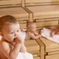SWO_BabySauna_132.jpg Drei Babys entspannen auf Holzbänken in einer Sauna; eines kaut auf einem Handtuch, zwei ruhen dahinter.Three babies relax on wooden benches in a sauna; one chews on a towel, two rest behind it.Drie baby's relaxen op houten banken in een sauna; één kauwt op een handdoek, twee rusten erachter.