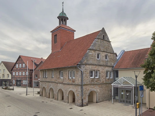 6-SMT-Wehnert_W1W2209-1.jpg Historisches Rathaus in Nienburg/Weser mit markanter Steinfassade und rotem Ziegeldach unter Wolkenhimmel.