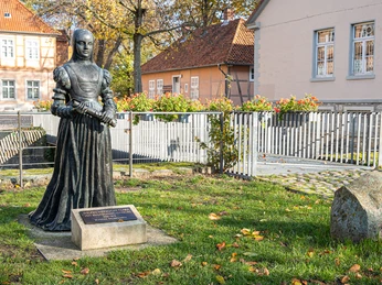 Bronzestatue einer Herzogin im Garten von Schloss Fallersleben vor Fachwerk- und Putzbauten.