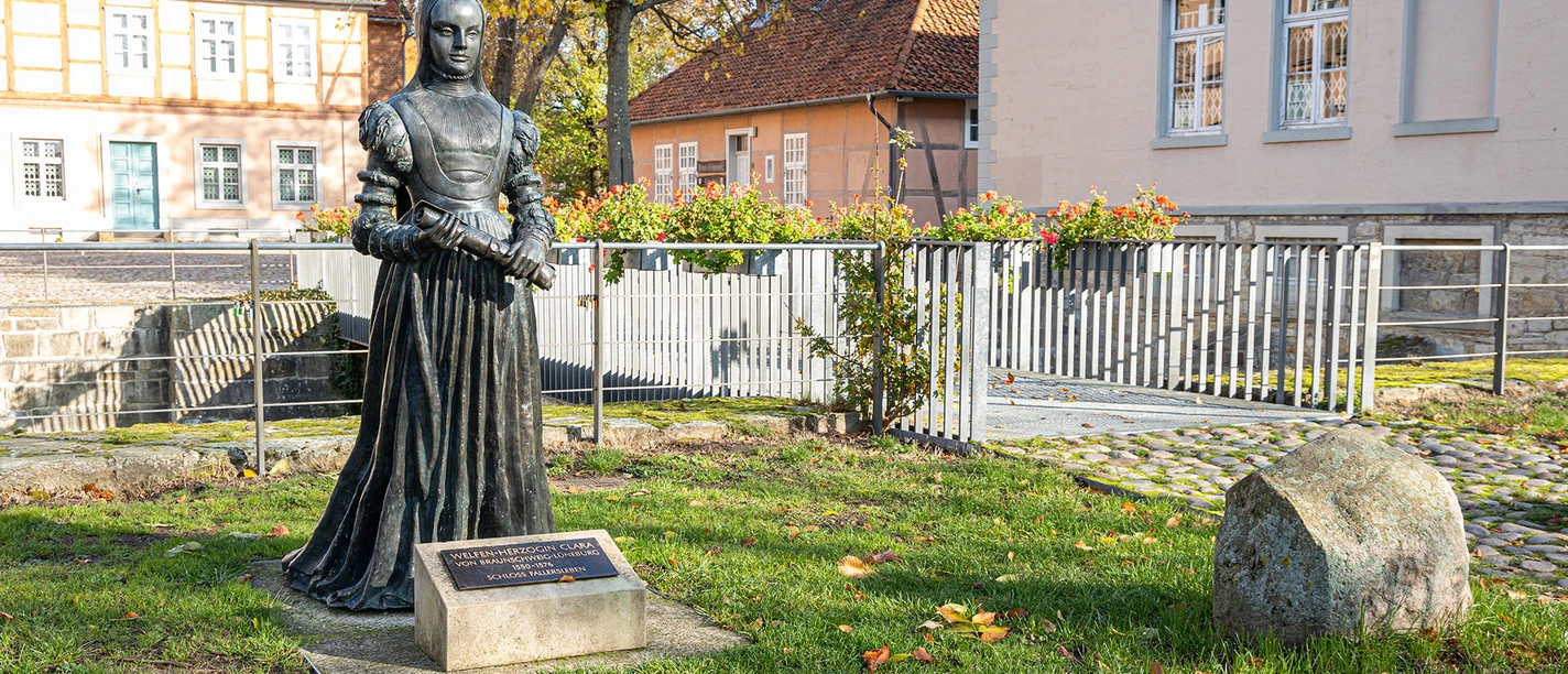 Bronzestatue einer Herzogin im Garten von Schloss Fallersleben vor Fachwerk- und Putzbauten.