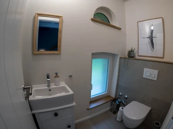 Kleines, modernes Badezimmer mit Waschbecken, WC, Fenster, Spiegel, Kunstbild und heller Beleuchtung.