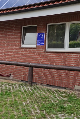 Behinderten-Parkplatz bei einem roten Backsteingebäude mit einem Holzgeländer im Vordergrund.